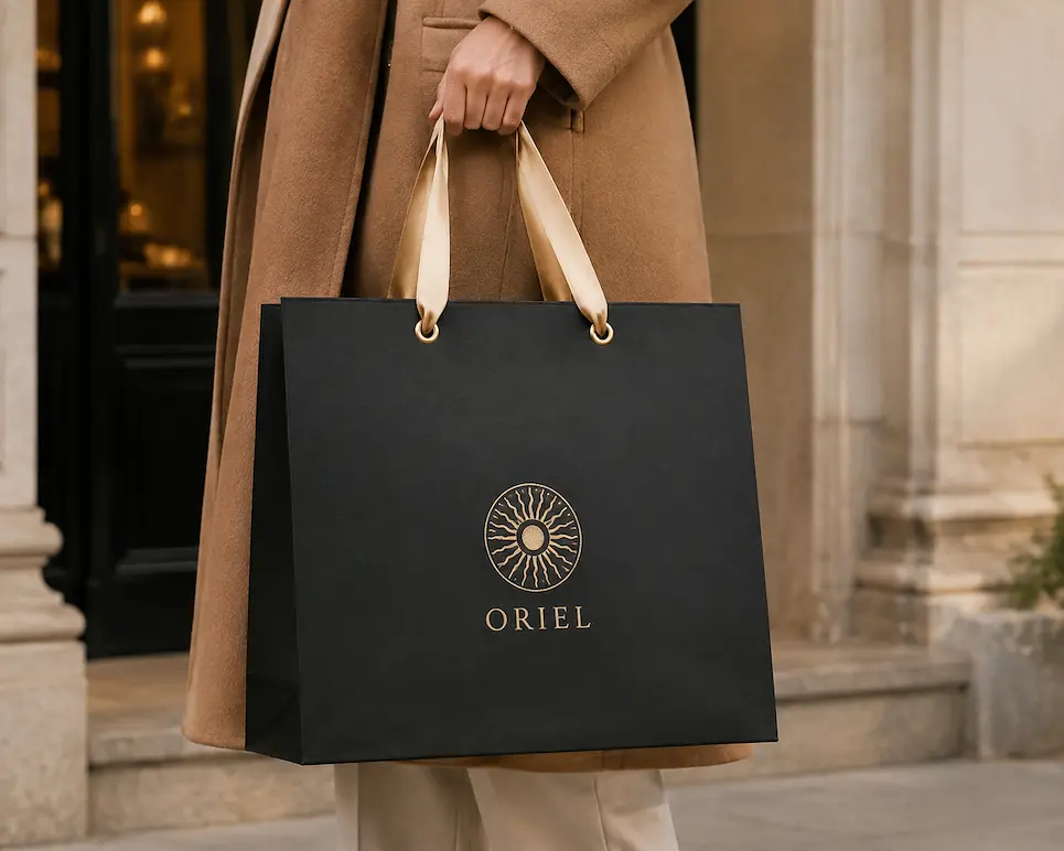 Green luxury bag with satin ribbon handles and a gold logo on a neutral background.